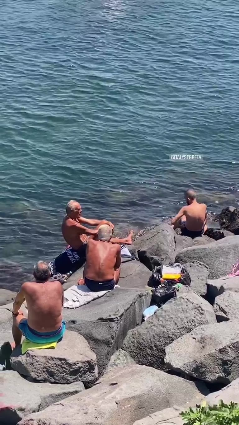 Locals sunbathing on Naples' rocky waterfront